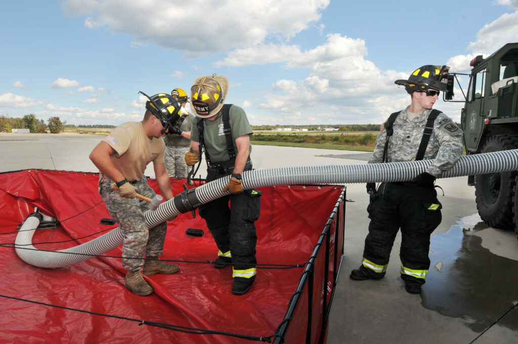 Firefighters training Army servicemen how to use a suction hose