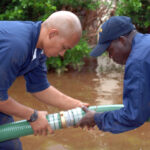 Two officers connect one suction hose to another during a flood.
