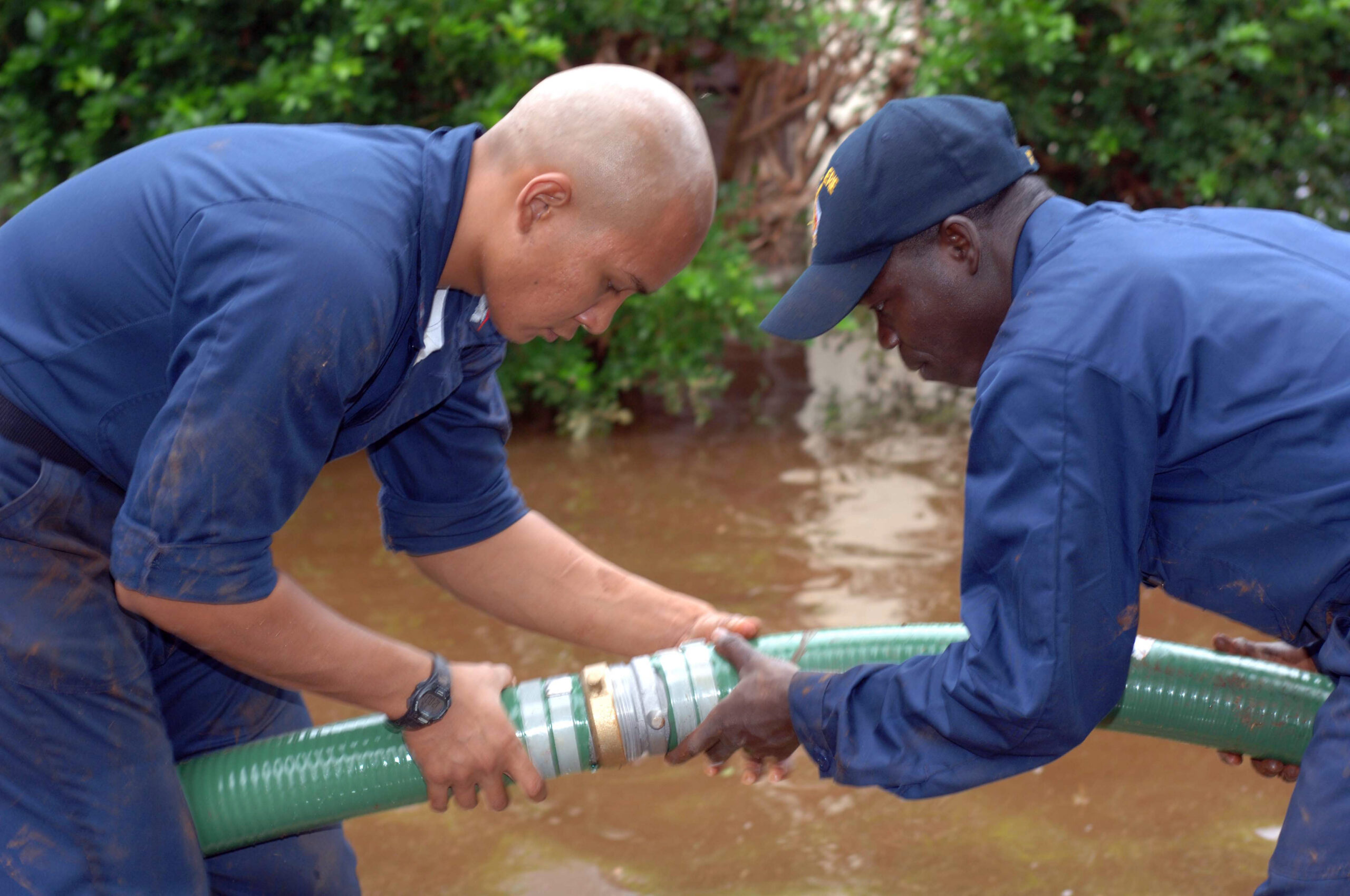 Two officers connect one suction hose to another during a flood.